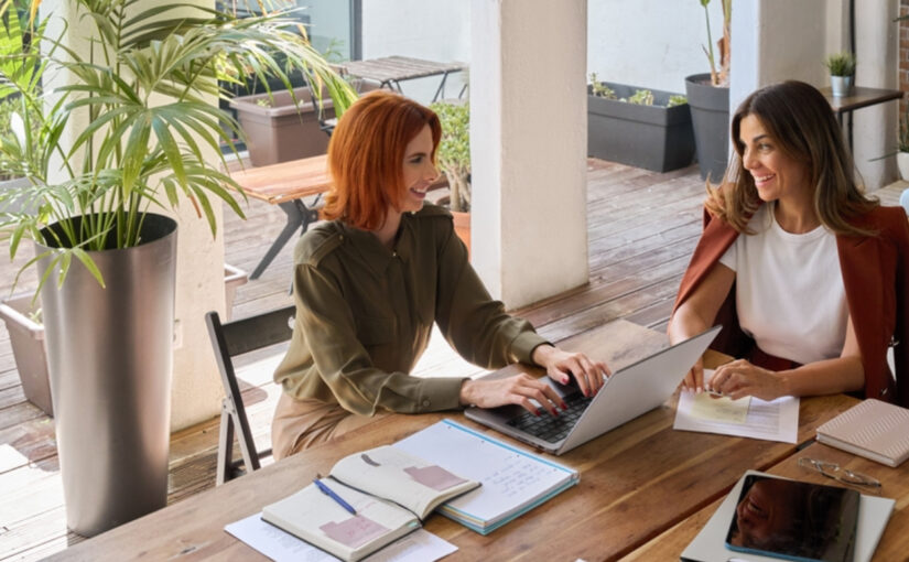 Professional women conversing at a desk with a laptop