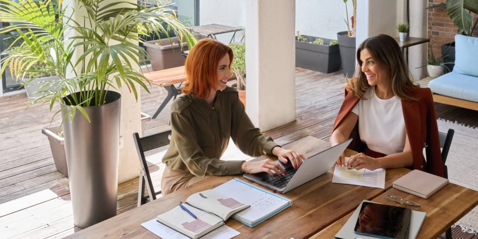 Professional women conversing at a desk with a laptop