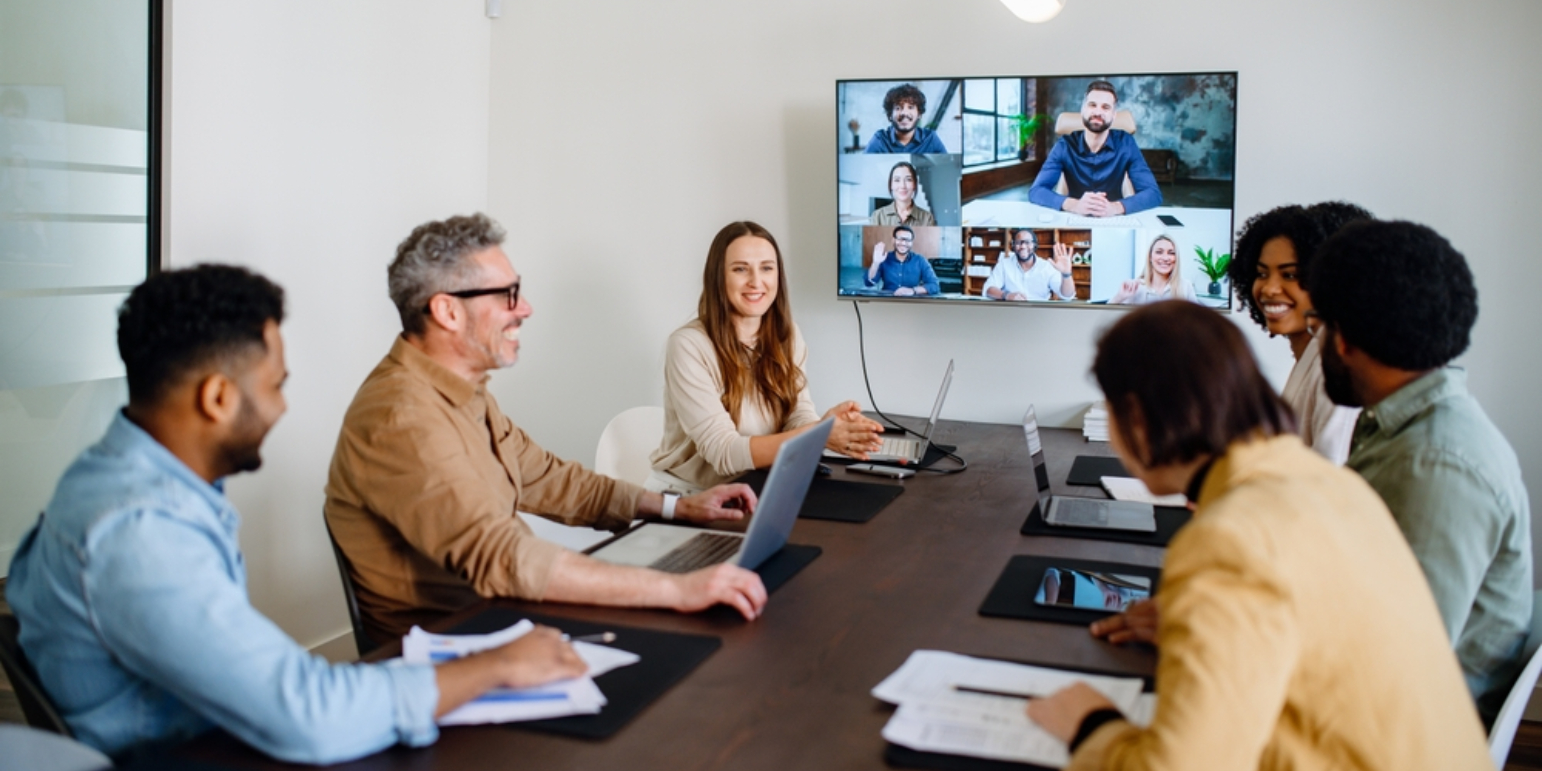 Group of professional office workers in a meeting room with hybrid workers on the screen